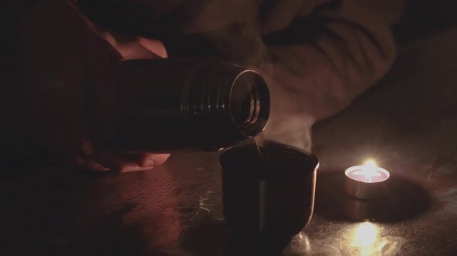 Pouring hot drink from thermos by candlelight during power outage