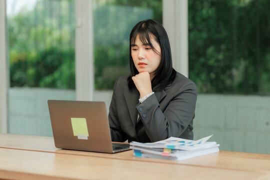 Young professional woman in an office, cross-referencing information from paper contracts with digital data on a screen, focusing on detailed vetting and accuracy.
