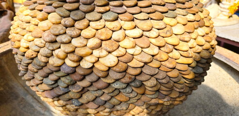 Decorating pots or jars with river stones. Garden decoration features stones with pattern resembling fish scales that sunlight. Stacked form shape of container and secured with cement for durability.  © Vanchuree