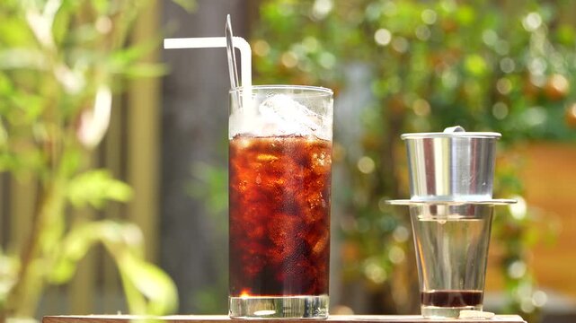 Traditional Vietnamese iced black coffee under golden sunrise light with phin filter background.