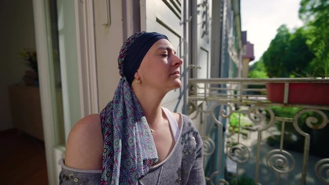 Woman undergoing chemotherapy on balcony lifting face toward sunlight expressing relief, resilience, hope and quiet healing during challenging life moment