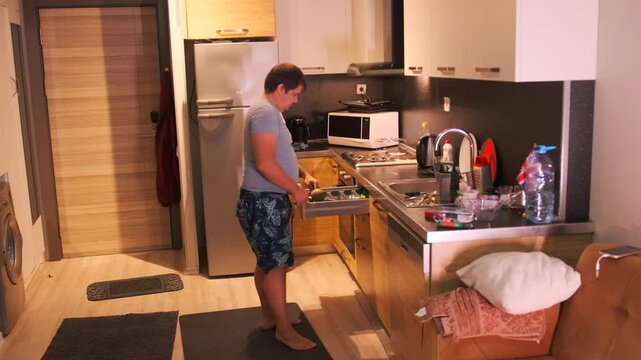 Man placing kitchen utensils into sliding drawer in modern kitchen, organizing cutlery and tools after washing, everyday domestic routine, maintaining order and cleanliness in home interior