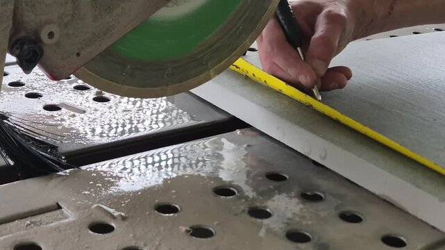Construction worker measuring and marking a tile slab before cutting with a wet saw.