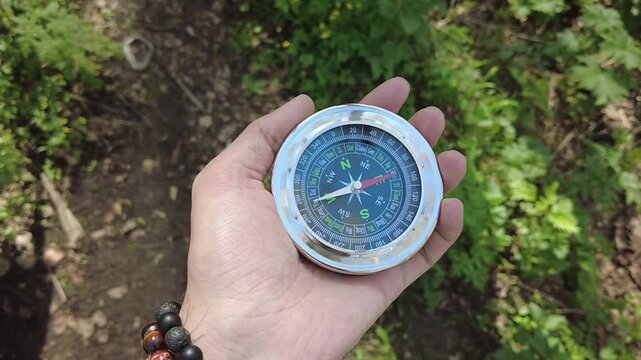 Hand holding magnetic compass in green mountain forest outdoor