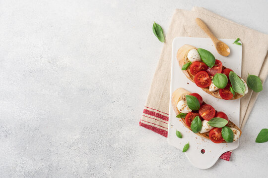 Bruschetta Caprese with cherry tomatoes mozzarella cheese and fresh basil on white ceramic board over light background, traditional Italian cuisine appetizer concept