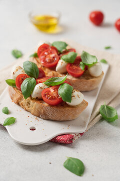 Bruschetta Caprese with cherry tomatoes mozzarella cheese and fresh basil on white ceramic board over light background, traditional Italian cuisine appetizer concept