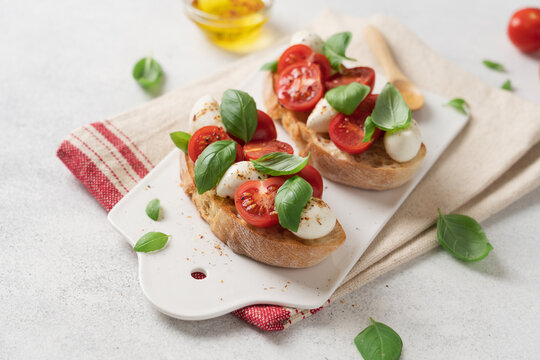 Bruschetta Caprese with cherry tomatoes mozzarella cheese and fresh basil on white ceramic board over light background, traditional Italian cuisine appetizer concept