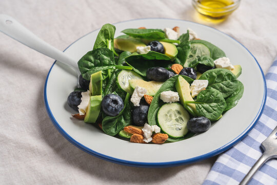 Healthy summer salad with avocado, spinach, almonds, cucumber, blueberries and feta cheese on linen tablecloth