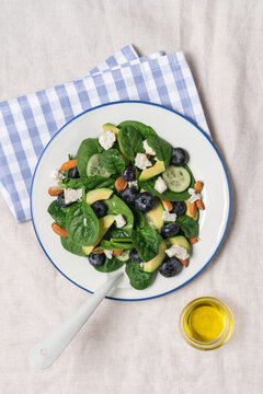 Healthy summer salad with avocado, spinach, almonds, cucumber, blueberries and feta cheese on linen tablecloth