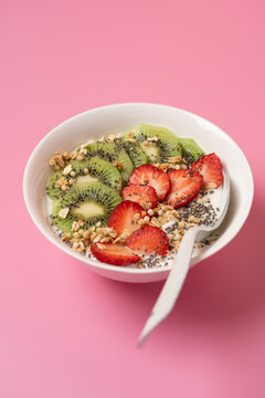 Protein breakfast with yogurt, chia seeds, strawberry and kiwi in white plate on trendy orange and pink background with copy space, healthy food concept