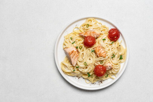Top view of spaghetti pasta with creamy sauce, salmon and tomatoes in white plate on light background with copy space, gourmet italian food