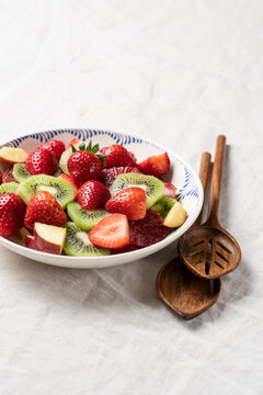 Fresh summer fruit salad with strawberries and kiwi in ceramic bowl on table with linen tablecloth, healthy seasonal dessert concept