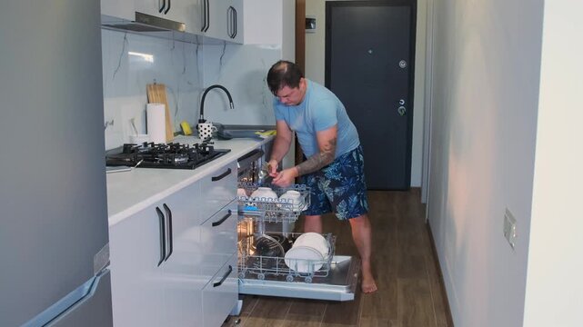 Man placing forks and spoons into dishwasher basket, organizing cutlery for washing. Kitchen cleaning routine focused on hygiene, order, and efficient use of household appliances