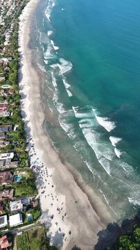 Imagem a&eacute;rea da Praia da Baleia com mar calmo, vegeta&ccedil;&atilde;o densa e casas pr&oacute;ximas &agrave; orla, representando destino tur&iacute;stico no litoral paulista com natureza preservada