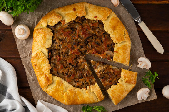 Savory galette or open pie with mushroom, onion and cheese on a dark wooden background. Rustic style. Top view.
