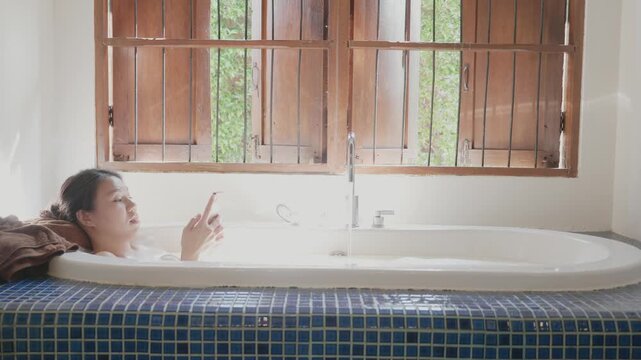 A serene scene of relaxation with a woman enjoying a bath in a well-lit bathroom, surrounded by natural light and wooden windows. Perfect for promoting tranquility and self-care.