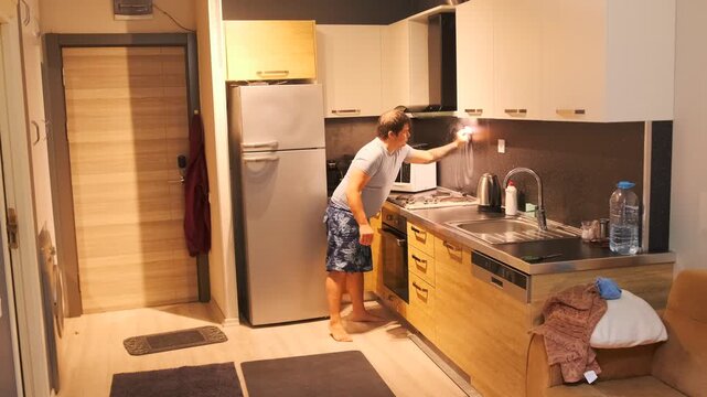 Man scrubbing kitchen backsplash with sponge and detergent, removing grease and stains from tiled wall near stove and sink, maintaining hygiene and cleanliness in modern apartment kitchen interior