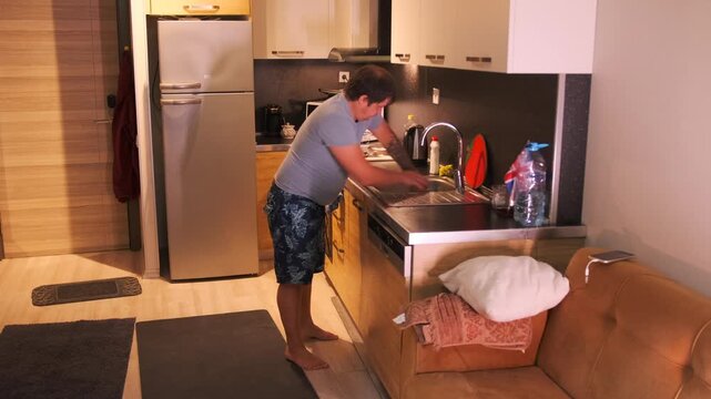 Man scrubbing kitchen sink with sponge and detergent, removing grease and food residue from metal surface, household cleaning routine, maintaining hygiene and cleanliness in modern home kitchen