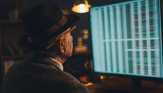 Elderly man in a fedora looking at stock market data on a computer screen at night in a dimly lit room
