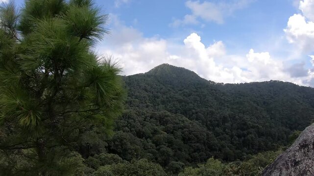 A breathtaking view of rolling green mountains under a partly cloudy sky. The lush forest enhances the natural beauty of the landscape, inviting outdoor enthusiasts to explore and enjoy nature's tranq