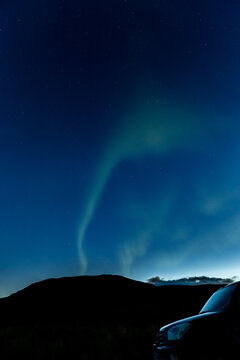 Arafed view of a car parked in a field with a bright green aurora behind it near Hvitserkur, Northern Iceland, long exposure motion blur