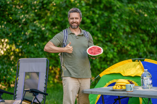 Man with watermelon in summer camping. Man hiker outdoor on summer day. Camp and nature picnic. Man camping show thumb up. Camp watermelon picnic. Yummy healthy food. Fresh food in camp