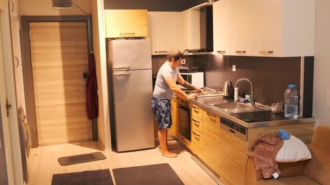 middle aged white man wiping stove surface medium view in kitchen, home cleaning routine using cloth, removing grease and stains, hygiene focused domestic task with everyday maintenance work