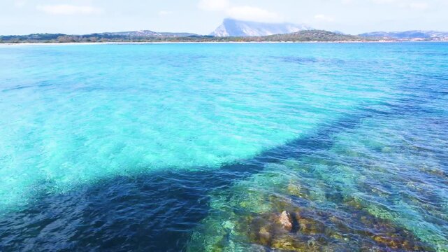 Aerial view of rocky coastline and deep blue sea at Lu Impostu beach in Sardinia, showing clear water gradients, coastal textures and Mediterranean landscape.