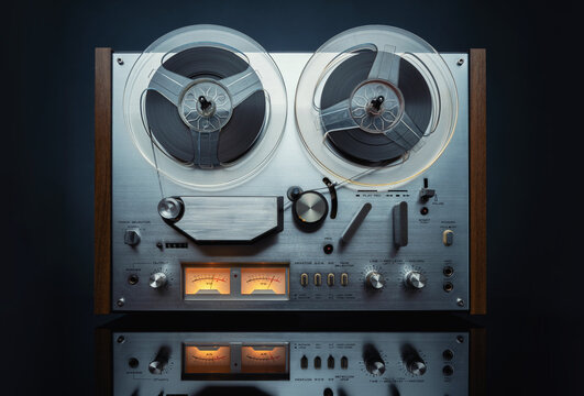 Vintage reel to reel tape recorder working on dark background, front view. Analog audio device with spinning reels and VU meters, classic retro technology, music recording concept