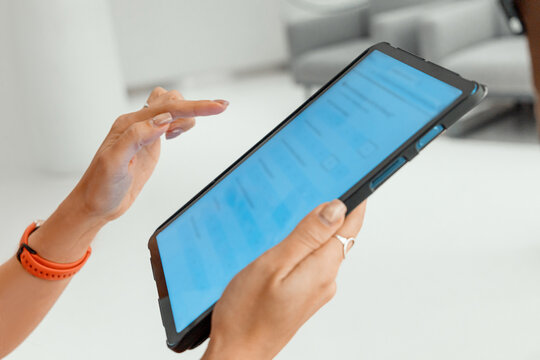 Woman holding and interacting with a digital tablet, navigating menus on the screen in a modern office environment