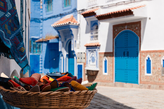 Colorful traditional babouche slippers and textile for sale in market street of blue painted Chefchaouen, Morocco