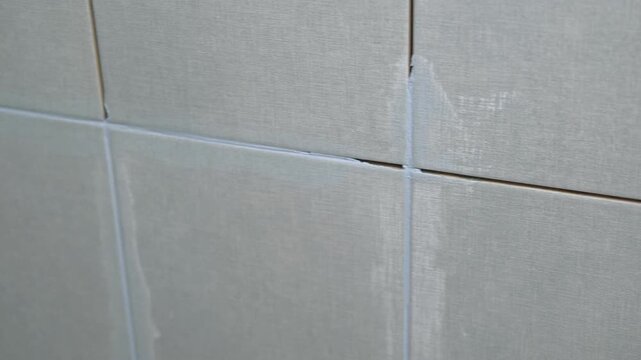Worker using a rubber grout float to smooth grout between tiles. Carefully applying sealant to tiles joints. Workman hands smoothing caulk, using small tool to remove excess and create clean seam.