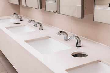 Fototapeta premium Multiple clean white sinks and automatic chrome faucets in a contemporary public bathroom, emphasizing hygiene and accessibility