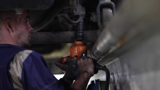 An expert mechanic clad in blue coveralls skillfully uses an air pistol to repair the suspension system of a truck, showcasing precision and expertise in automotive maintenance.