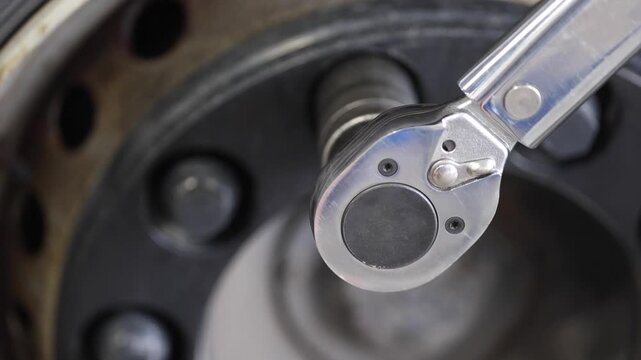 This image features a professional mechanic at a service shop, expertly unscrewing a truck wheel. His focus and usage of a large tool emphasize the intricate work involved in automotive maintenance.
