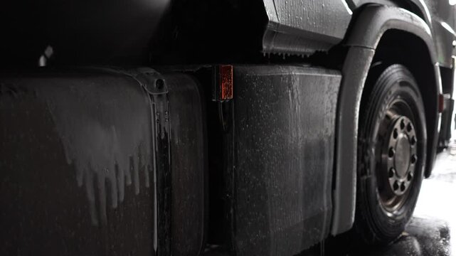 An expert car washer is seen using professional equipment to wash the wheels of a sizable truck, demonstrating the importance of using water and foam in achieving a thorough clean for heavy vehicles.