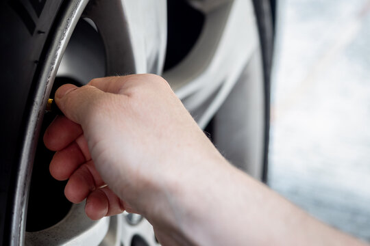 Close-up of a hand screwing a cap onto a car tire valve on an alloy wheel - concept of vehicle maintenance, tire inflation and safety check