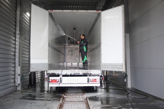A dedicated professional truck cleaner thoroughly washing a semi-trailer truck. Water sprays reflect sunlight, highlighting the meticulous effort put into making the truck shine like new.