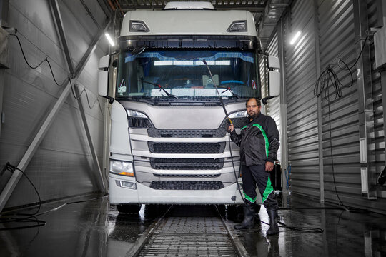 A professional cleaner stands confidently beside a white truck, holding a non-contact washing gun. This image showcases cleanliness and efficiency as the cleaner prepares to ensure a spotless finish.