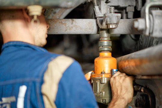 An expert mechanic clad in blue coveralls skillfully uses an air pistol to repair the suspension system of a truck, showcasing precision and expertise in automotive maintenance.