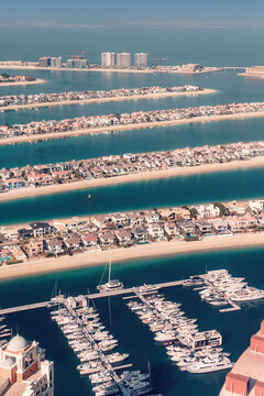 Aerial view discovering Palm Jumeirah artificial archipelago, with luxury villas, modern hotels, and yachts docked in the marina