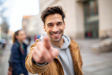 Obraz premium Professional scene of smiling man pointing finger at camera while walking with friend on city street, bright urban environment softly blurred, natural daylight for social media