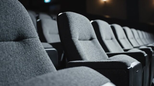 This shows a row of empty gray seats in a darkened press conference room. The seats are neatly arranged in rows, with a blurred background that adds to the ambiance of the setting.