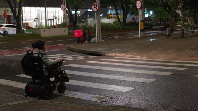 Motorized Wheelchair User Crossing Road at Night with Cars Passing, Night Life and Accessibility