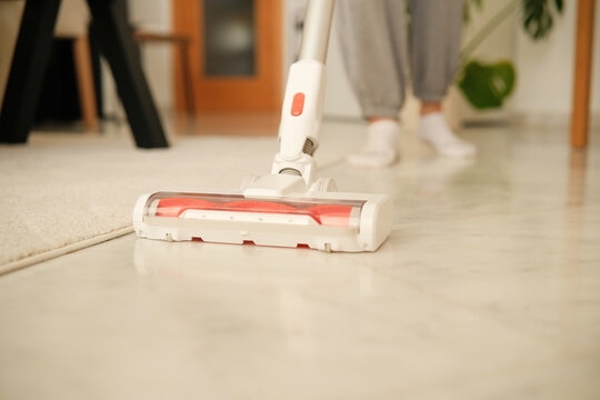 Woman vacuums marble floor with modern white vacuum cleaner. Household chores, daily home routine, everyday maintenance