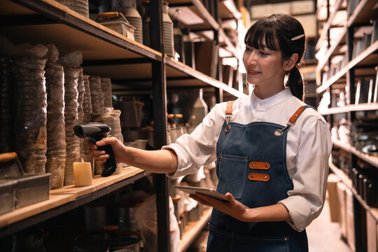 Woman working in warehouse, scanning shelf inventory with tablet and handheld barcode scanner, organized storage aisle