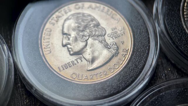 Close up video of the front side of a 1999 United States Washington Quarter coin featuring the obverse portrait of George Washington inside a protective capsule.