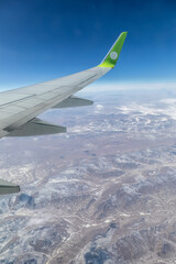 Obraz premium The visible part of an airplane wing over snow-capped mountain peaks. Airplane flight