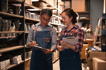 Naklejka premium Warehouse worker clipboard inventory shelf storage logistics interior teamwork asian adult female male apron uniform inspection planning record document paper pen aisle industry stockroom retail