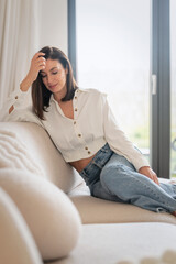 Fototapeta premium Portrait of an elegant woman relaxing on a couch in her bright, minimalist home